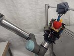 The UR5e robot arm with a custom gripper attachment grasping a fake 3D printed apple.